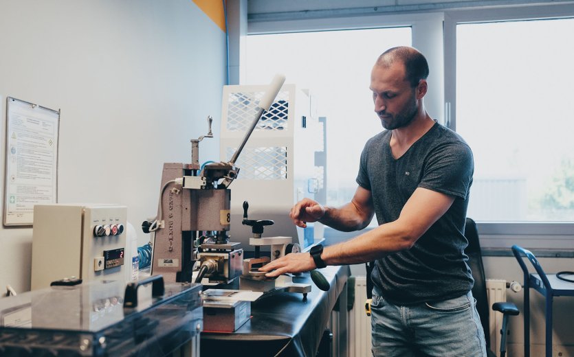 La photo montre une machine de test pour les matériaux des sacoches. L'un des employés la commande.