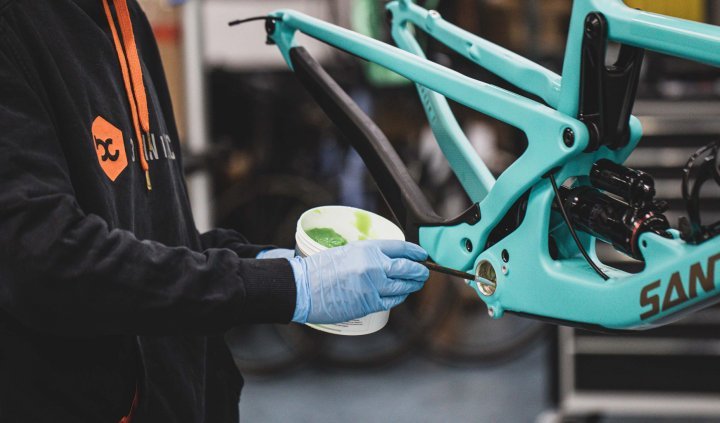A mechanic is greasing the bottom bracket shell of a Santa Cruz mountain bike.