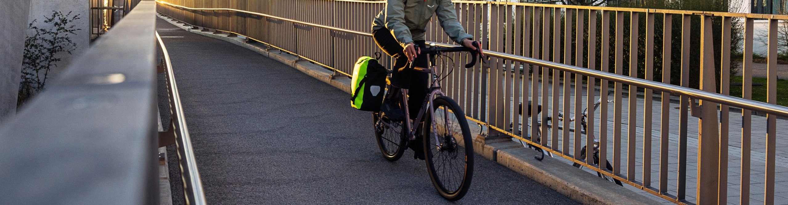 Radfahrerin mit wasserdichter ORTLIEB Fahrradtasche am Gepäckträger fährt über eine Brücke in der Stadt