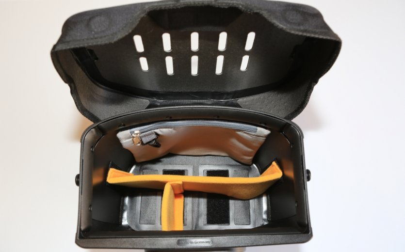 The interior of a black bicycle bag with multiple compartments, including a padded area, a small zippered pocket, and an orange divider.