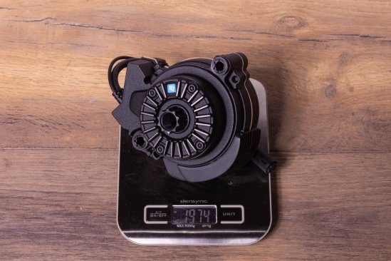 A TQ HPR60 e-bike drive on a kitchen scale on a dark wooden floor. Display shows 1,974 grams