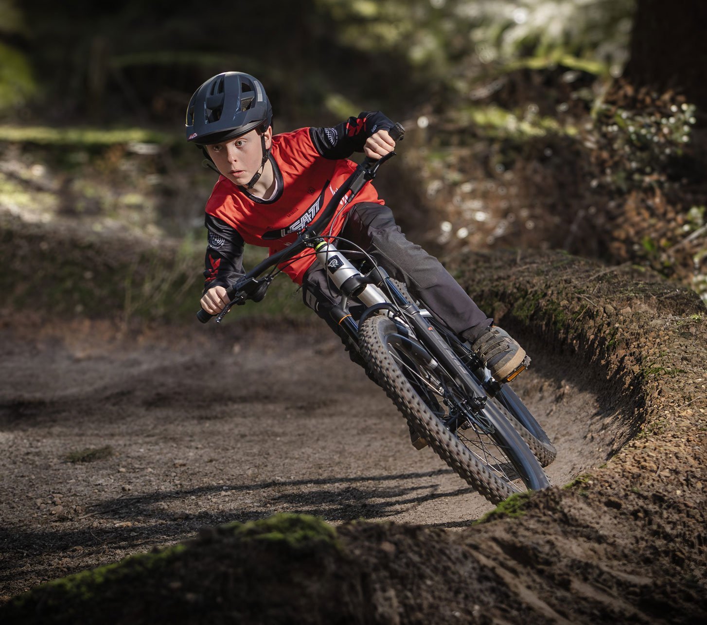 Kind fährt mit einem Early Rider Kinder Mountainbike dynamisch durch eine Waldkurve auf dem Trail
