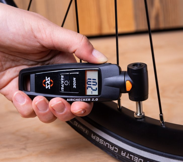 Close-up photo: A woman's hand holds an SKS pressure gauge against a bicycle valve.
