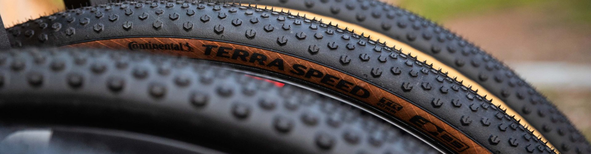 Gros plan de plusieurs pneus de gravel avec profil marqué et flancs beiges, superposés, mettant en avant la structure et la bande de roulement.