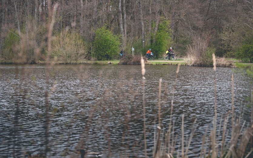 3 Teilnehmer des Events auf einer flachen Schotterpassage am Ufer eines Sees. 