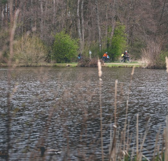 3 Teilnehmer des Events auf einer flachen Schotterpassage am Ufer eines Sees. 