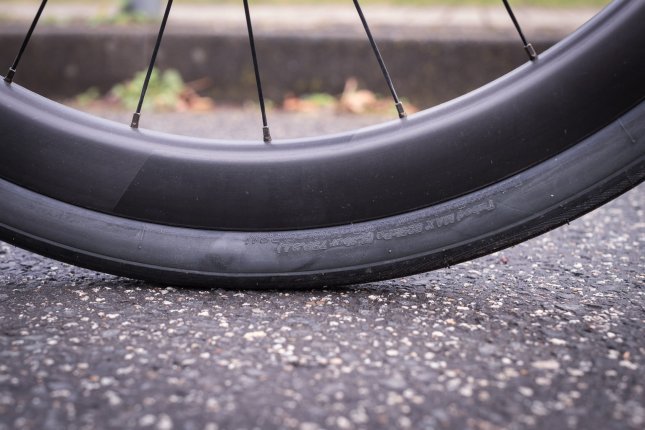 Detailfoto: Ein Rennrad-Laufrad steht auf Asphalt. Wir sehen den unteren Teil des Reifens, bei der Aufstandsfläche.