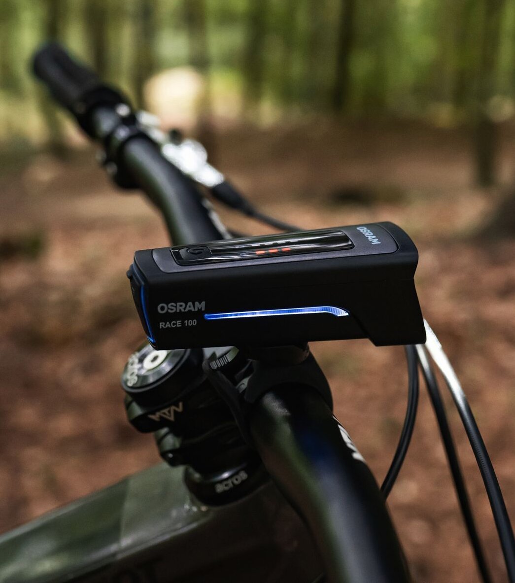 OSRAM Race 100 bike light on the handlebar – detail shot with forest background