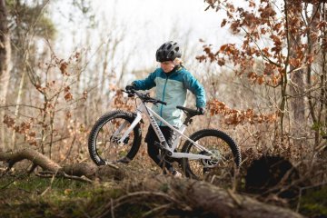 Child pushing a lightweight kids bike over an obstacle in the forest, highlighting the importance of low weight for control and handling.