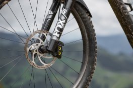 Front wheel of a mountain bike with disc brake and FOX suspension fork, blurred landscape in the background.