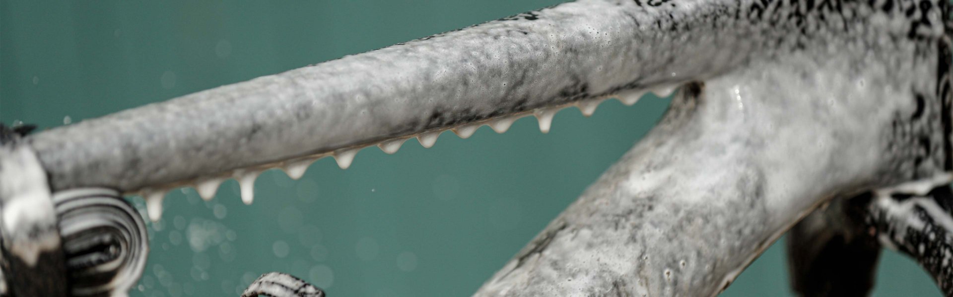 Nahaufnahme eines Fahrradrahmens, der mit Reinigungs­schaum bedeckt ist. Schaum tropft vom Oberrohr herab, während der Rahmen auf einem Montageständer fixiert ist.