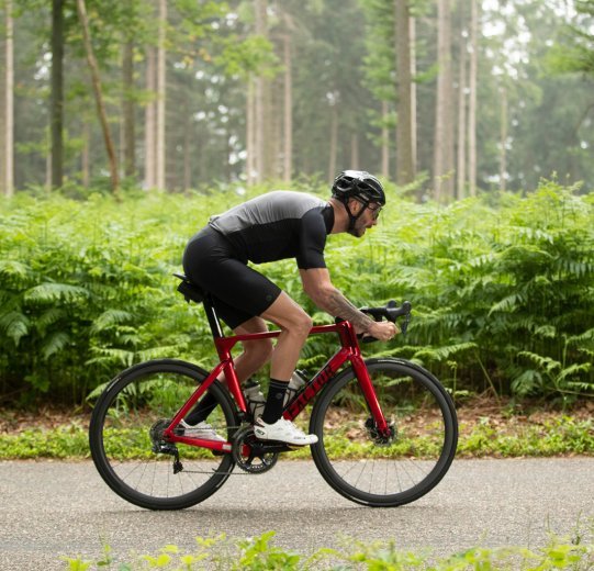 Un coureur cycliste roule sur une route à travers la forêt. Il conduit un Factor One.