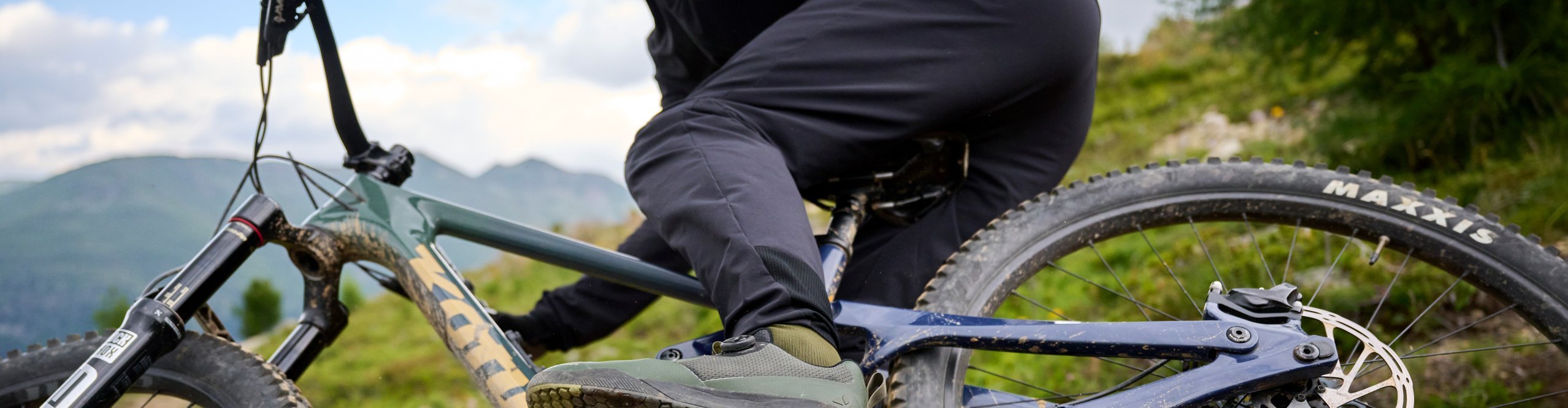 Nahaufnahme eines Mountainbikes mit Maxxis-Reifen und Flatpedals sowie VAUDE Hose – bereit für alpines Terrain.