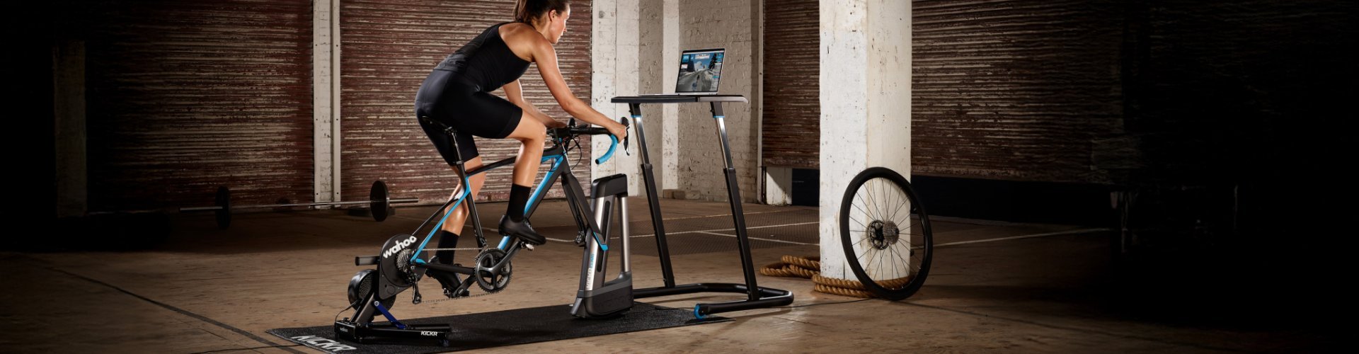 Persona pedaleando en un rodillo inteligente de interior mientras mira un portátil con software de entrenamiento.