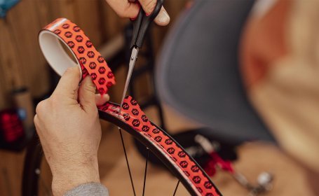 Hand schneidet das aufgeklebte Felgenband mit einer Schere rund ab, um einen sauberen Abschluss zu formen.
