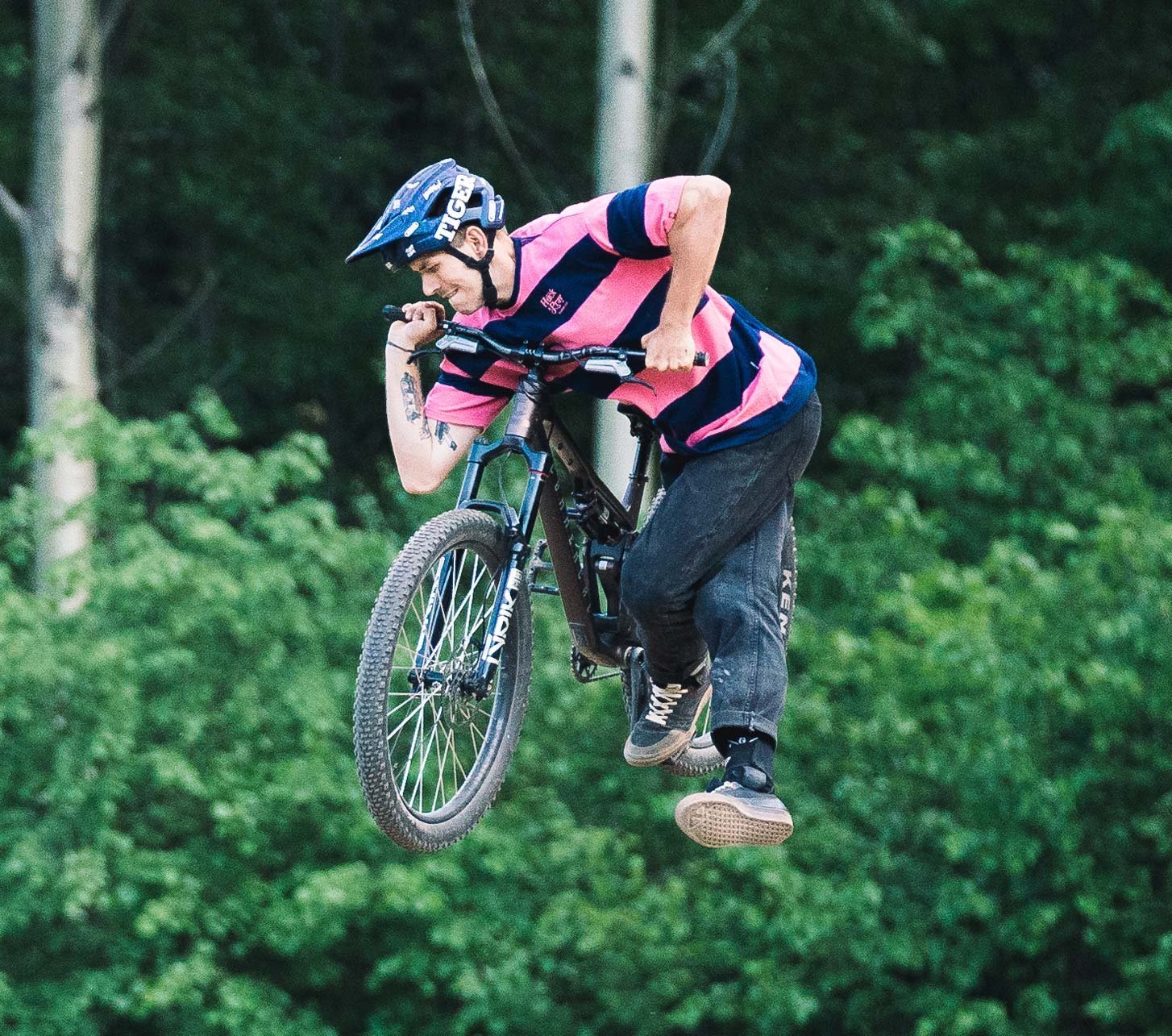 Mountain biker wearing Loose Riders apparel performing a jump on a trail mountain bike in the forest