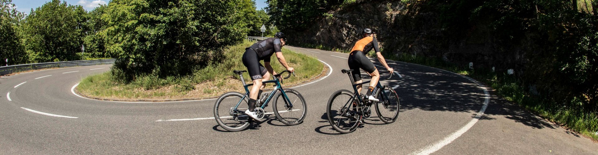 Two road cyclists, both on Specialized Tarmac SL7 bikes, are passing uphill on a winding road.