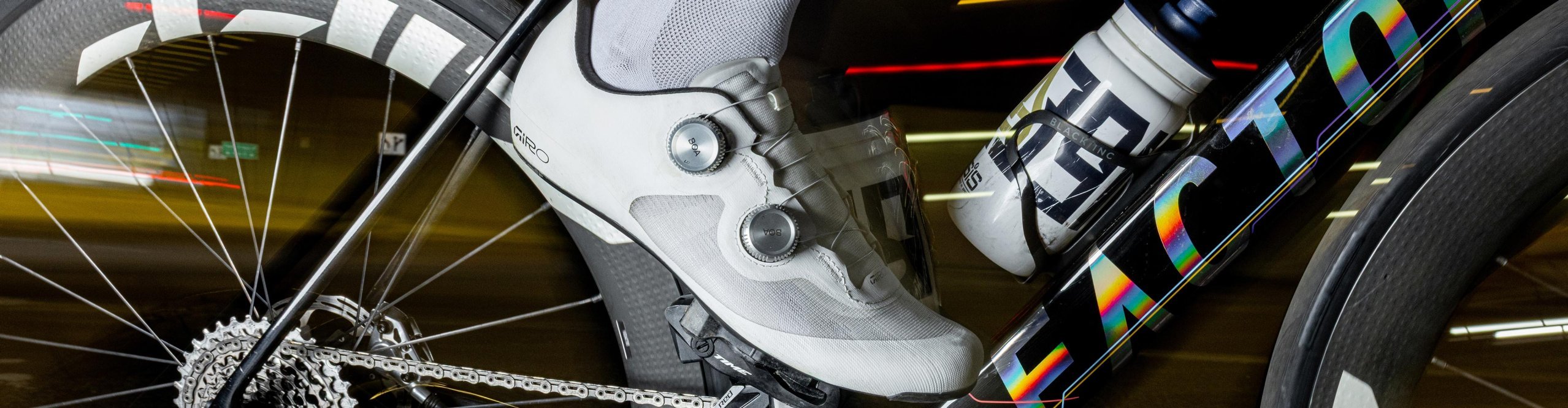 Ciclista de carretera con zapatillas de ciclismo blancas Giro enganchadas al pedal de una bicicleta Factor Ostro con bielas SRAM y rueda de carbono