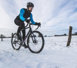 Un hombre en una bicicleta gravel pedalea por un paisaje nevado.