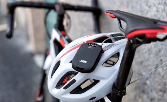 Candado de cable compacto con combinación pasado por las aberturas de un casco de bicicleta y sujeto a la bici.