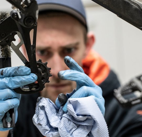 Thomas, mécanicien chez bc, nettoie le galet inférieur du dérailleur arrière avec une serviette en papier bleue.