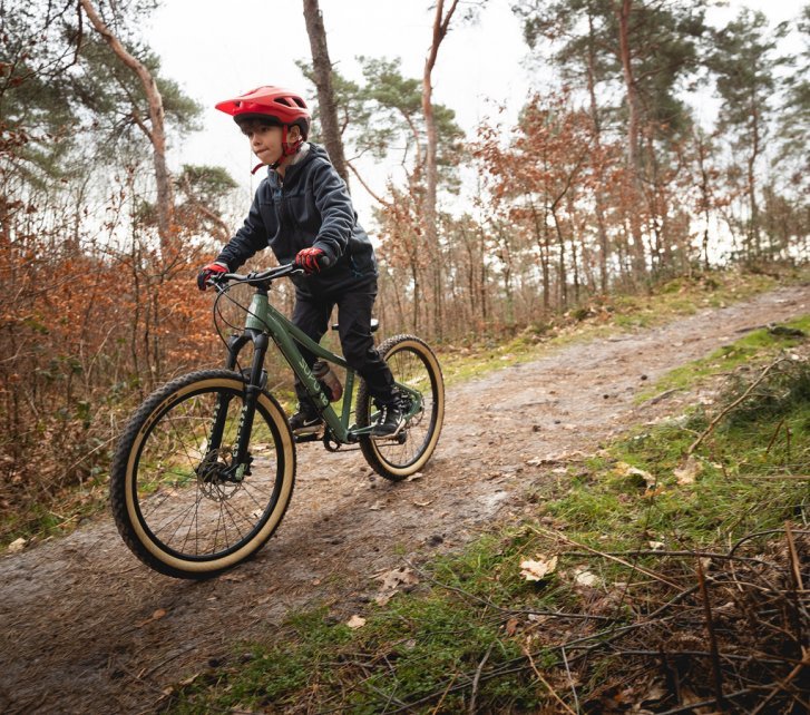 A boy rides a SUPURB bike with suspension fork down a forest path. 