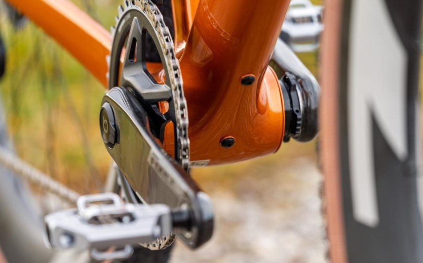 Close-up of the drivetrain and bottom bracket on an orange OPEN U.P. gravel bike with flat pedal.