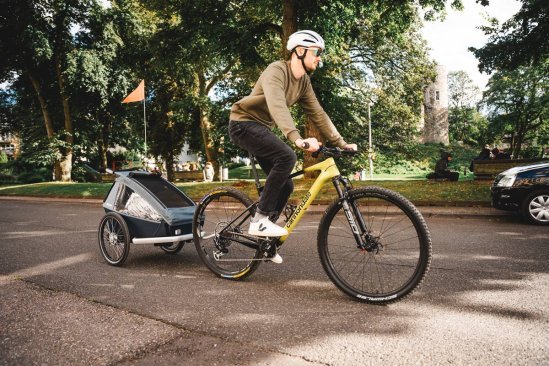 Cyclist towing a bike trailer on the road as an alternative to a child bike seat for transporting kids.