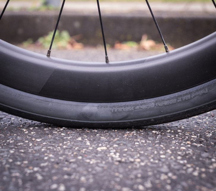 Detailfoto: Ein Rennrad-Laufrad steht auf Asphalt. Wir sehen den unteren Teil des Reifens, bei der Aufstandsfläche. 