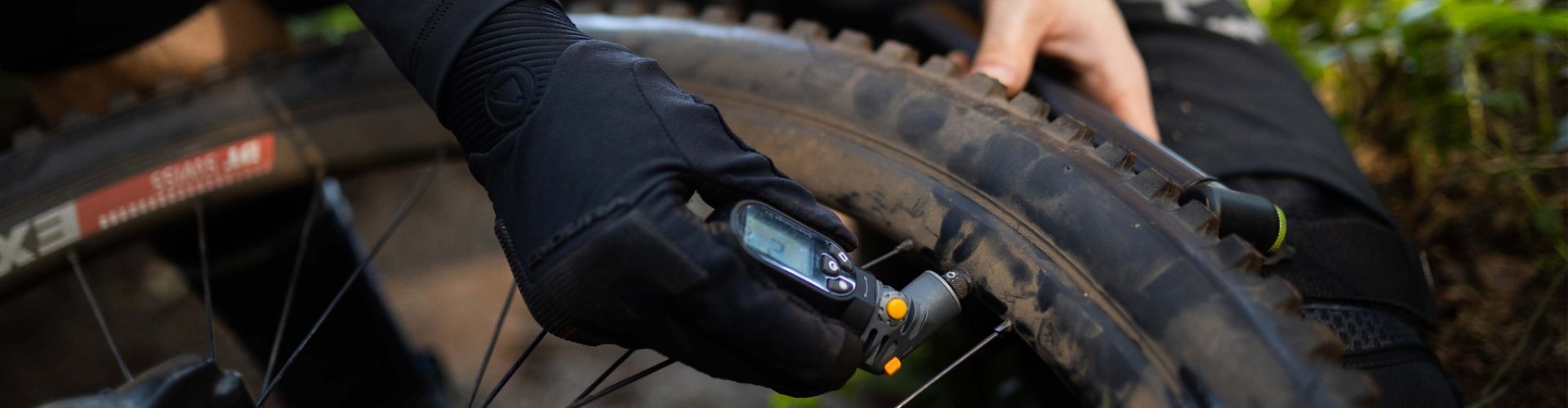 Ciclista de montaña midiendo la presión de un neumático de MTB con tacos usando un medidor digital.
