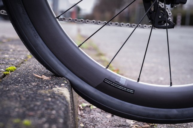 Detailfoto: Das Hinterrad eines Rennrades rollt einen Bordstein hoch. Man sieht, wie der Reifen von der Steinkante in Richtung Felge eingedrückt wird.