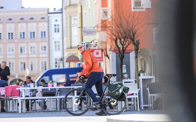 Radfahrer mit ORTLIEB-Tasche hält in einer belebten Fußgängerzone mit Straßencafés.