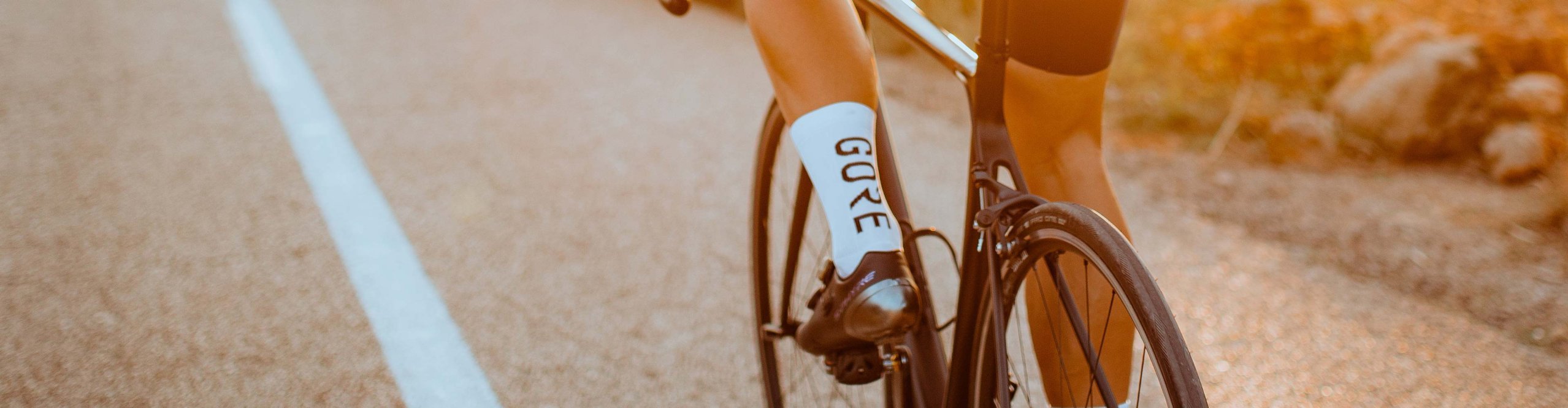 Ciclista de carretera con calcetines de ciclismo Gore Wear blancos montando en bicicleta de carretera al atardecer
