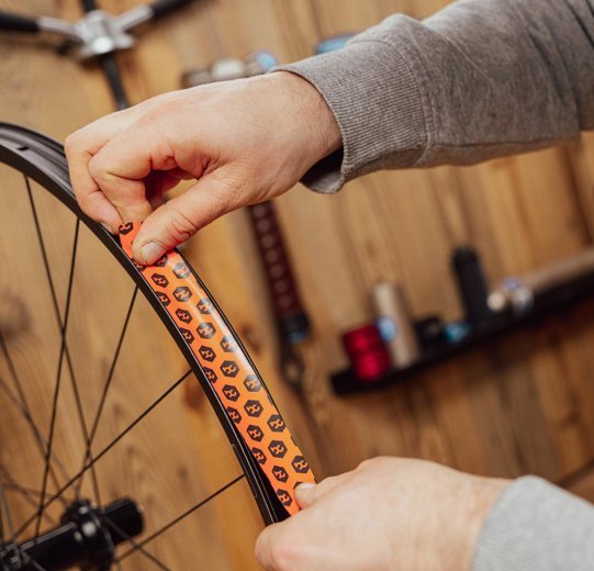 Main posant un fond de jante dans une jante de vélo, en commençant quelques centimètres avant le trou de valve.