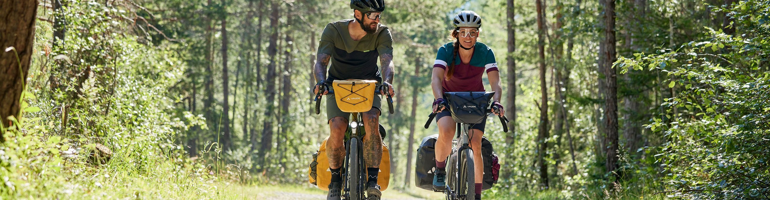 Zwei Radreisende auf Schotterweg im Wald mit kompletter Vaude-Taschenausrüstung – Naturgenuss und Outdoor-Feeling pur