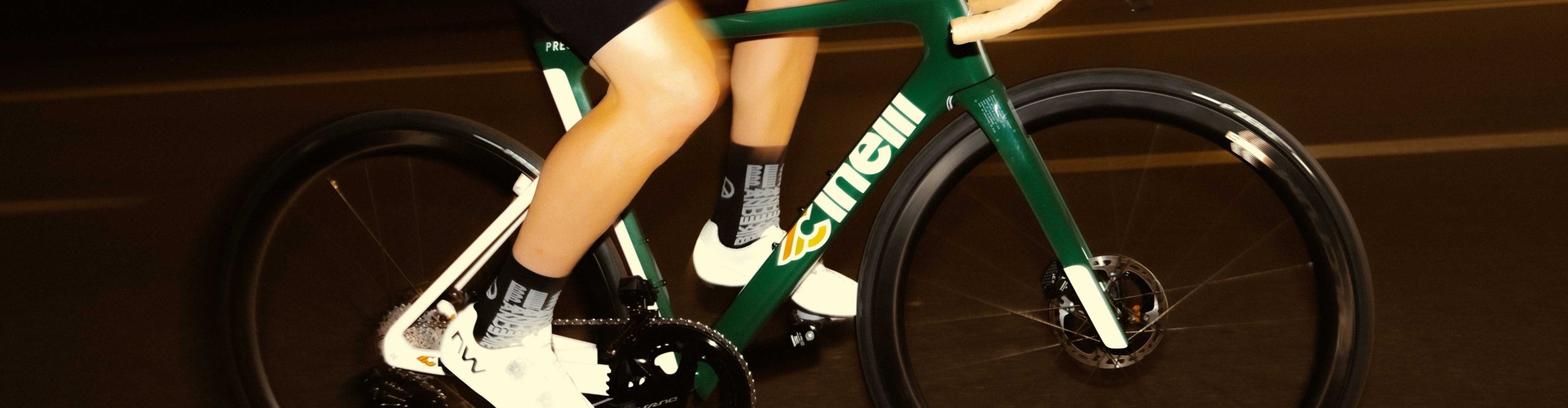 Detailaufnahme eines grünen Cinelli Pressure II Rennrads in Fahrt mit Motion Blur, Fokus auf Rahmen, Kurbel und Laufräder.