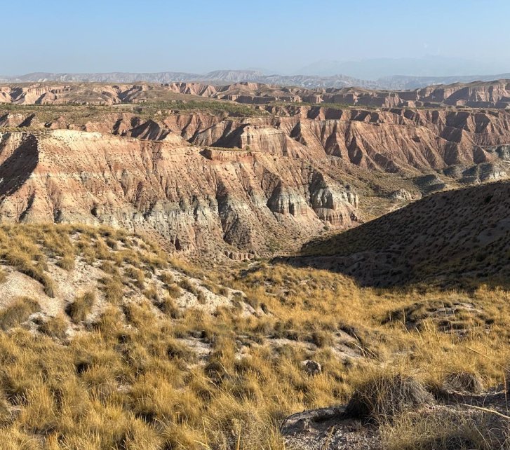 Totale einer Erosionslandschaft in der Spanischen Wüste. Man erkennt eine Bänderung der Steilhänge durch die Schichtung verschiedenfarbiger Gesteine. Der Himmel ist wolkenlos blau