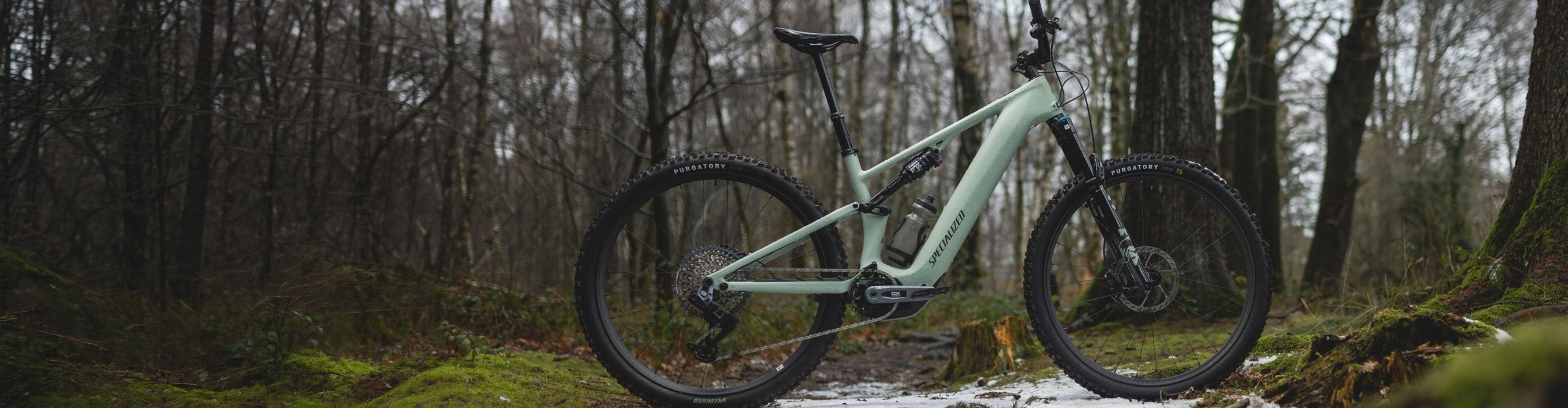 Nouveau VTT électrique Specialized Turbo Levo R tout-suspendu vert menthe, vue de profil sur un sentier en forêt