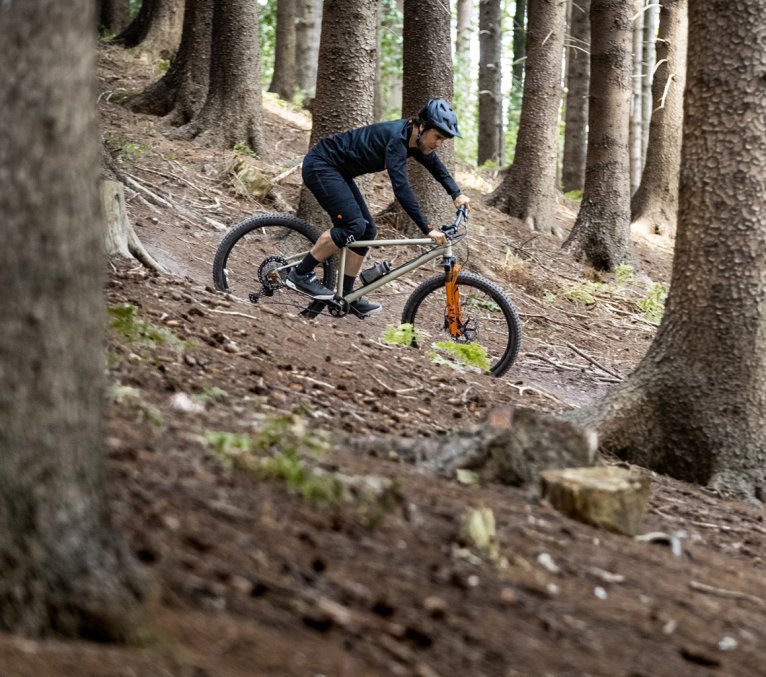 Ein Mountainbiker fährt auf einem bc original Podsol einen Trail in einem Wald herunter.