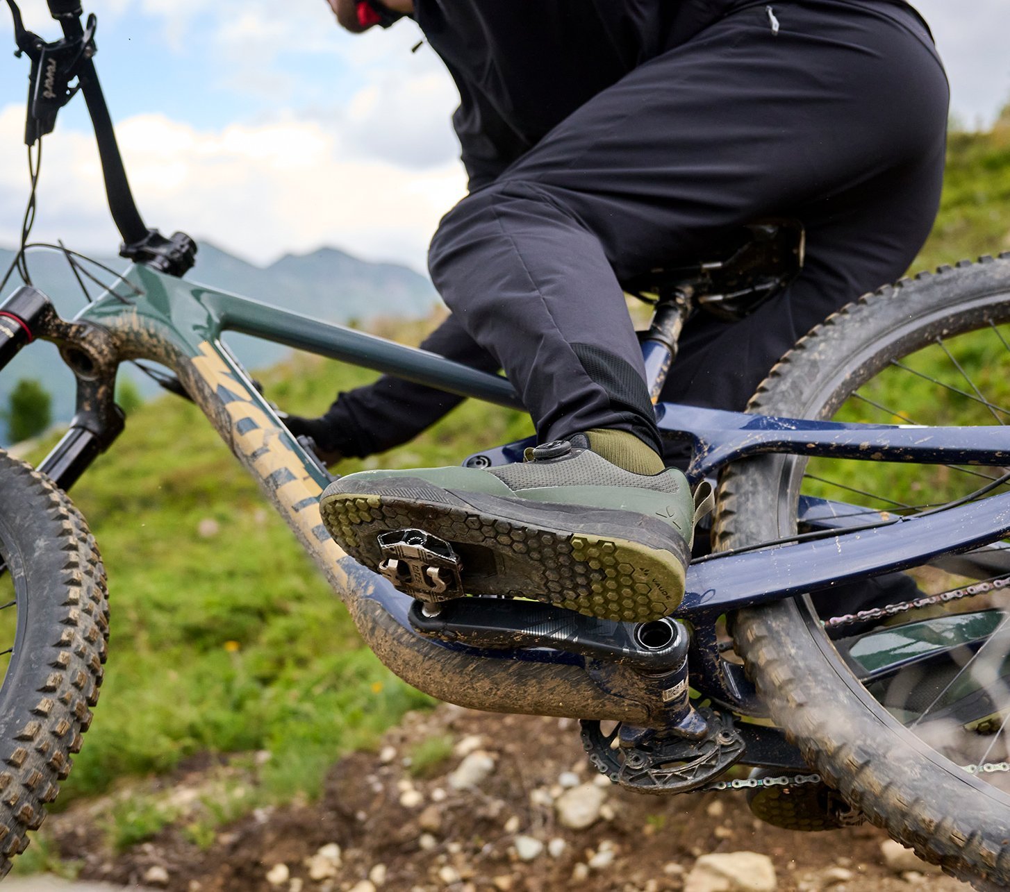 Nahaufnahme eines Mountainbikes mit Maxxis-Reifen und Flatpedals sowie VAUDE Hose – bereit für alpines Terrain.