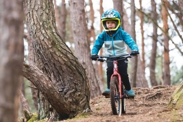 Child riding a kids mountain bike on a forest trail wearing a full face helmet for added protection on challenging terrain.