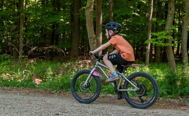 A girl rides an Early Rider through the forest. Her bike also has fenders and lighting.