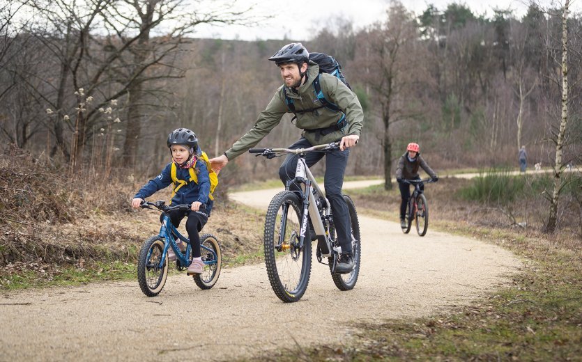 Ein Kind fährt mit dem SUPURB BO16 einen Trail im Wald und wird geschoben