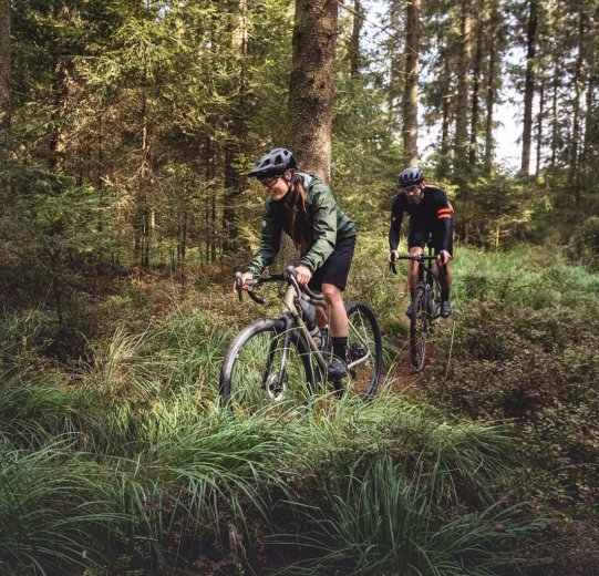 A man and a woman ride their gravel bikes along a forest path.