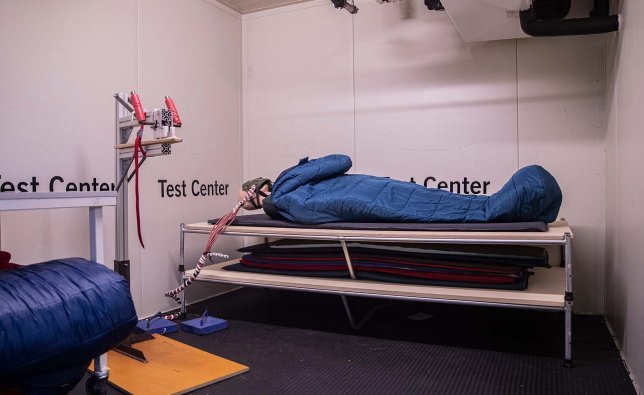 A standard mannequin lies in a VAUDE sleeping bag in a controlled climate chamber at the VAUDE Test Centre. The heat loss of the doll is being measured.