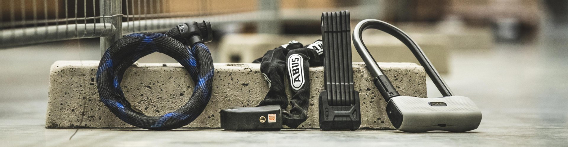 Varios candados para bicicleta – de cable, cadena, plegable y en U – colocados uno junto a otro sobre un bloque de hormigón en entorno urbano.