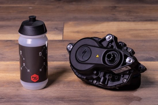 A Specialized 3.1 e-bike drive on a dark wooden floor. Next to it is a bike water bottle
