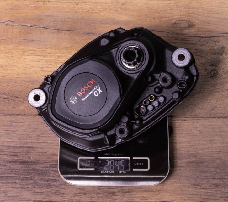 A Bosch CX e-bike drive on an electronic kitchen scale on a dark wooden floor. Display shows 2,845 grams