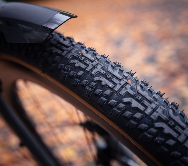 Detail shot: a gravel tyre tread with autumn leaves softly blurred in the background.