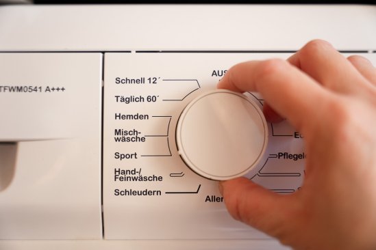 Das Programmwahlrad einer Waschmaschine. Eine Hand stellt das Sportprogramm ein.